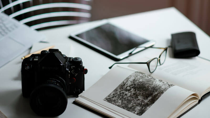 arts Reading glasses, camera, and an iPad rest on a table representing pieces of the process when planning a custom travel itinerary.