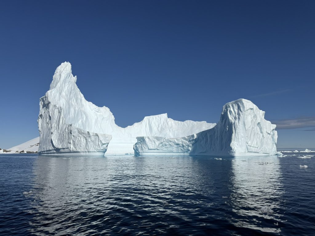 A large iceberg, in the shape of a caldera, floats in the ocean on a sunny day. Image taken by the author while visiting Antarctica in February 2025.