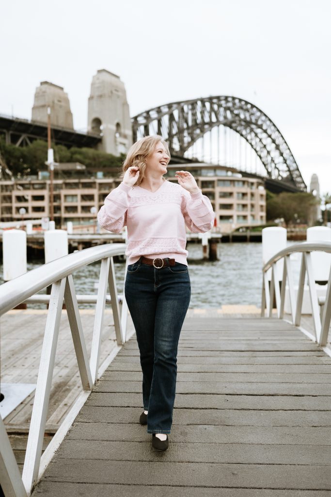 Photo of the author walking over a wooden bridge with the Sydney Harbour Bridge in the background on her 3-day Sydney itinerary. Photo taken by an Airbnb Experience photographer.