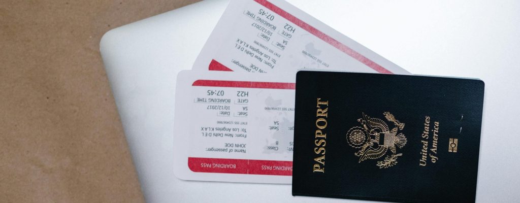 Image of a closed laptop with a US passport and boarding passes on top. Photo used to illustrate working while traveling and 5 business travel tips to add vacation into your work trips. Photo by RDNE Stock project