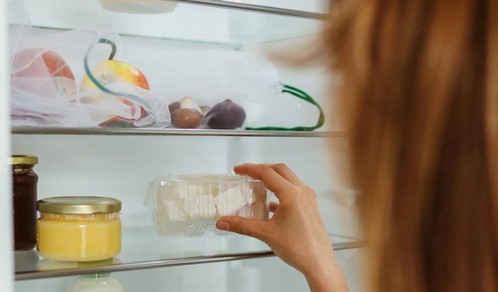 Lady is inspecting an item in her fridge before she leaves on a trip. Part of the important pre-departure travel checklist. Photo by Polina Tankilevitch